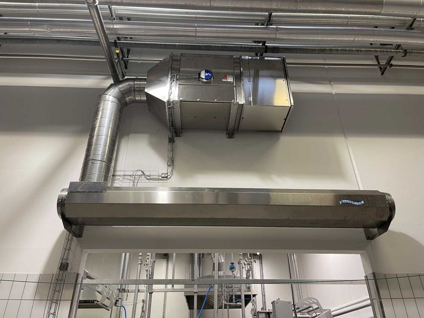 Rostfri Masterveil AS-K luftrid&aring; installerad ovanf&ouml;r en d&ouml;rr&ouml;ppning i en livsmedelsmilj&ouml;, ansluten till ventilationskanaler f&ouml;r att bevara kall luft och minska energif&ouml;rluster.