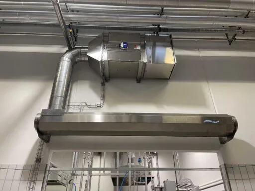 Stainless steel Masterveil AS-K air curtain installed above a doorway in a food processing environment, connected to ventilation ductwork to preserve cold air and reduce energy loss.
